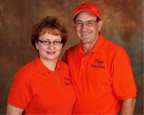 A man and woman wearing matching orange shirts and caps, smiling against a textured brown background.