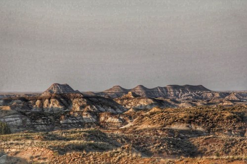 A panoramic view of rugged, layered hills under a hazy sky, showcasing the natural beauty of a desert landscape.
