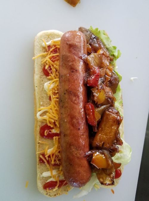 A hot dog on a bun topped with cheese, lettuce, ketchup, mayonnaise, and sautéed vegetables.