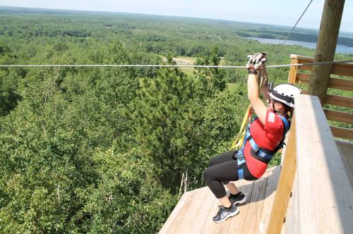 A person in a helmet and harness zip-lining from a platform, surrounded by trees and a scenic landscape.