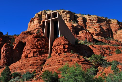 A modern building set against red rock formations under a clear blue sky, surrounded by greenery.