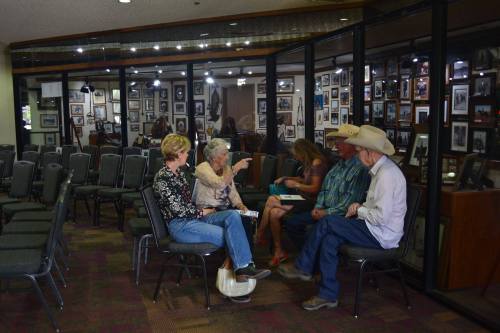 A group of four people seated in a room filled with framed photos, engaged in conversation.