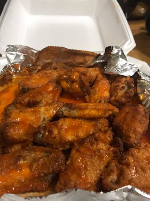 A tray of crispy chicken wings coated in spicy orange sauce, served in a takeout container.