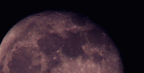 Close-up view of the moon's surface, showcasing craters and texture against a dark background.