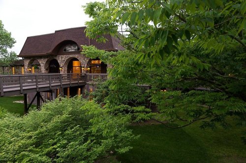 A stone building with a sloped roof surrounded by lush greenery and trees, featuring a wooden deck.