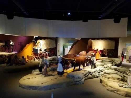 A museum exhibit featuring covered wagons, oxen, and figures in historical attire on a rocky landscape.