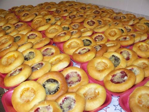 A large display of round pastries with various fruit fillings arranged on pink plates.