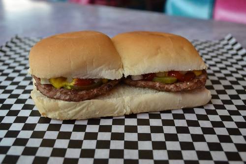 Two mini burgers with pickles, ketchup, and mustard on a checkered paper background.