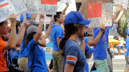 A crowd of supporters in blue shirts and hats holds signs cheering for the Gators at a parade.