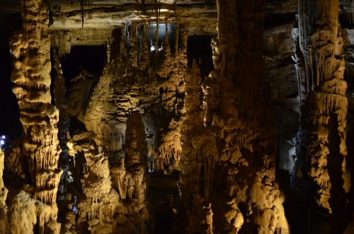 Stalactites and stalagmites in a dimly lit cave, showcasing intricate rock formations and textures.