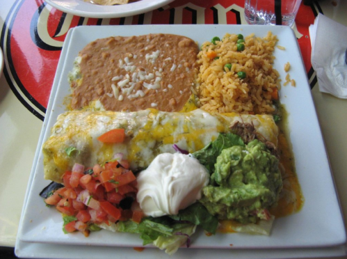 A plate of enchiladas with rice, refried beans, guacamole, sour cream, and fresh vegetables.