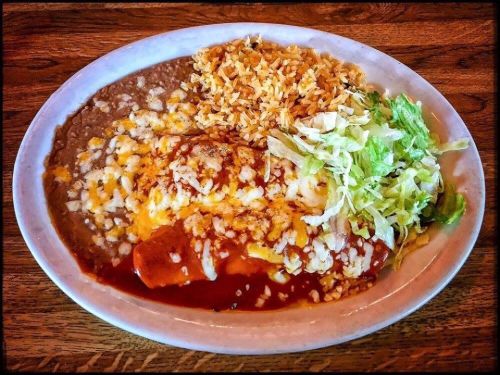 A plate of enchiladas topped with cheese and sauce, served with rice, refried beans, and shredded lettuce.
