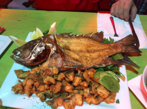 A whole fried fish served on a platter with lemon wedges and a side of fried seafood.