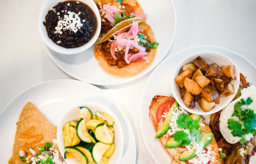 A vibrant spread of tacos, black beans, roasted potatoes, and sautéed zucchini on white plates.