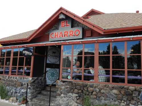 Exterior of El Charro restaurant featuring a stone facade and large windows, with diners visible inside.
