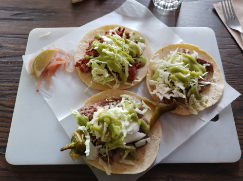 Three tacos on a white plate, topped with meat, green sauce, cabbage, and a slice of lime on the side.