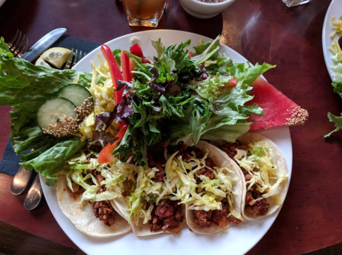 A plate of tacos filled with meat and topped with shredded lettuce, accompanied by a fresh salad and watermelon slices.