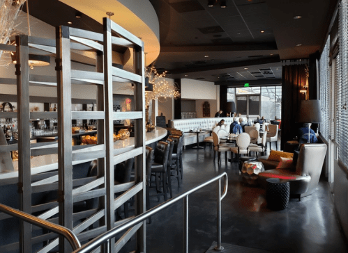 A modern restaurant interior featuring a bar, seating areas, and decorative lighting, with patrons dining.