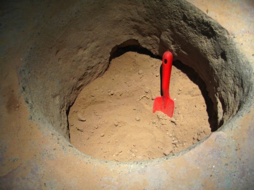A small red shovel rests in a circular hole filled with brown dirt.