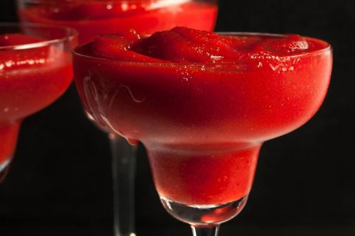 Three vibrant red frozen cocktails in elegant glasses against a dark background.