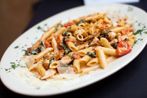 A plate of penne pasta with chicken, spinach, and tomatoes, garnished with herbs and cheese.