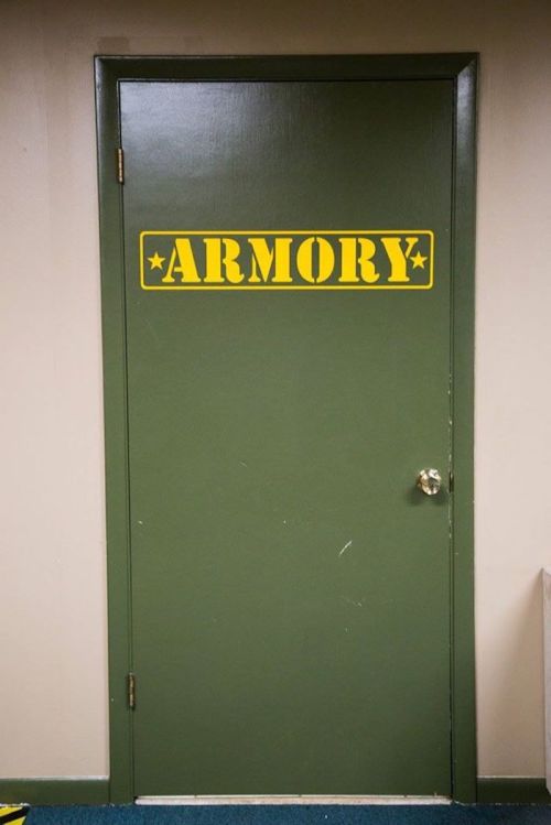 A green door labeled "ARMORY" in bold yellow letters, with a simple doorknob.
