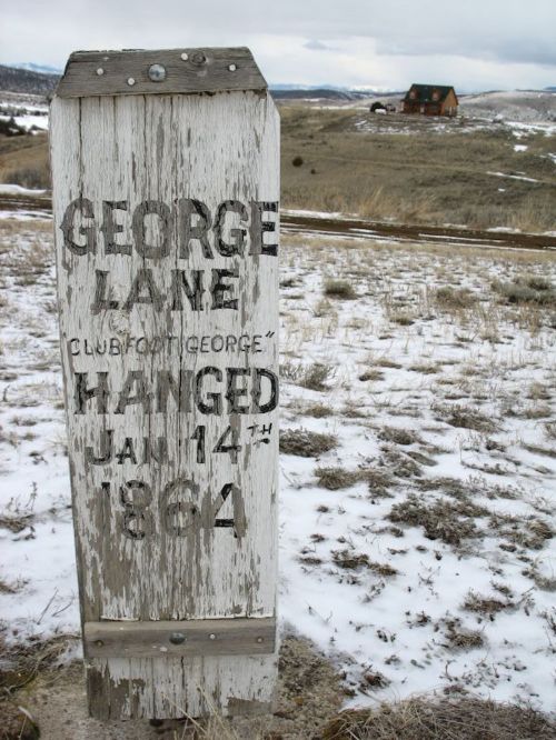 Weathered sign marking the hanging of George Lane on January 14, 1864, with a distant house and snowy landscape.