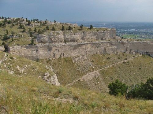 A scenic view of rugged cliffs and grassy slopes under a cloudy sky, with a distant landscape visible.