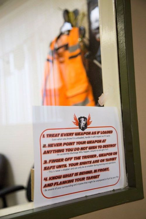 A safety poster on a wall with firearm handling rules, emphasizing caution and awareness around weapons.