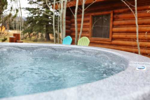 A close-up of a hot tub with bubbling water, set against a rustic log cabin and colorful outdoor chairs.