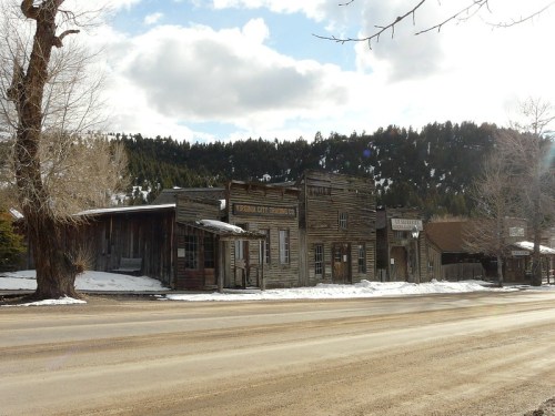 A historic wooden building in a snowy landscape, with mountains and clouds in the background.