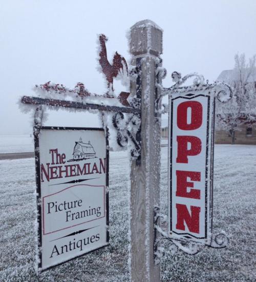A frosty sign for "The Nehemian" featuring "Open" and "Picture Framing Antiques" in a snowy landscape.