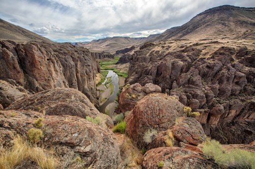 A scenic view of a winding river surrounded by rugged cliffs and rocky terrain under a cloudy sky.