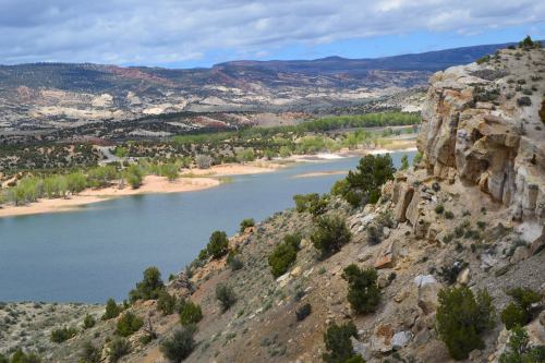 A scenic view of a river winding through a landscape of hills and rocky cliffs, with greenery along the water's edge.