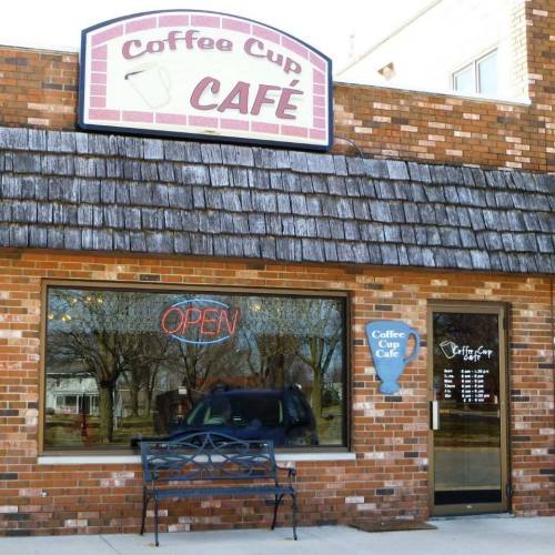 Exterior of Coffee Cup Café featuring a brick facade, shingled roof, and an "OPEN" sign in the window.