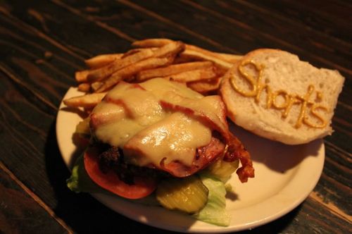 A plate with a cheeseburger topped with lettuce, tomato, and pickles, served with fries and a bun labeled "Short's."