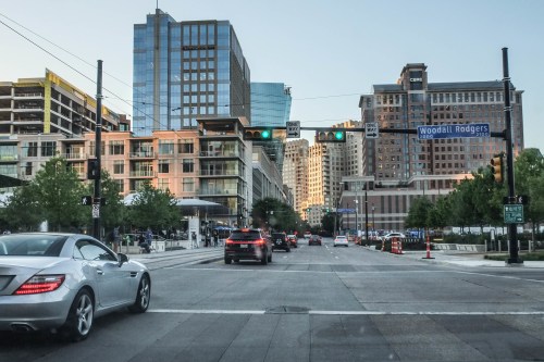 City street scene with modern buildings, traffic lights, and cars on the road, under a clear blue sky.