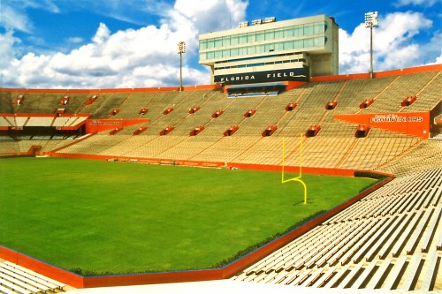 A wide view of a football stadium with empty seats and a bright blue sky filled with clouds.