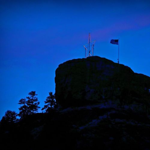 A glowing star and flag atop a rocky hill against a deep blue twilight sky.