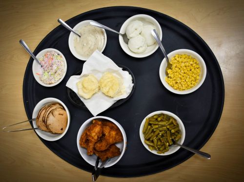 A black tray with bowls of food: fried chicken, green beans, corn, coleslaw, mashed potatoes, and biscuits.