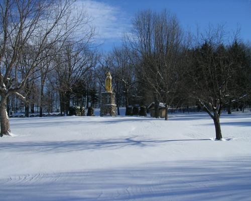 A snow-covered landscape with bare trees and a statue in the distance under a clear blue sky.