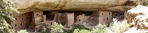 Ancient cliff dwellings nestled under a rock overhang, surrounded by greenery.