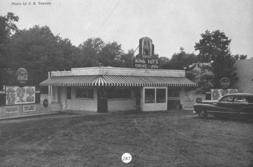 Black and white photo of King Tut's Drive-In, featuring a striped awning and vintage cars parked outside.