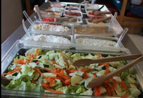 A variety of salad ingredients displayed in trays, including lettuce, cucumbers, carrots, and various toppings.