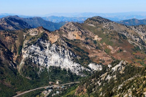 A panoramic view of rugged mountains with rocky slopes and lush greenery under a clear blue sky.