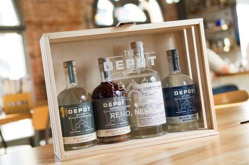 A wooden display case featuring four bottles of whiskey and gin from The Depot, labeled with their names and origins.