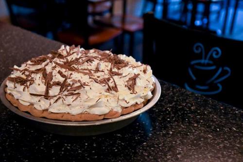 A chocolate cream pie topped with whipped cream and chocolate shavings, sitting on a dark countertop.