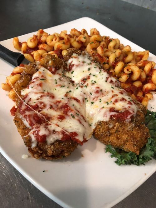 A plate featuring two breaded chicken cutlets topped with marinara sauce and melted cheese, served with pasta.