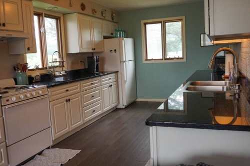A bright kitchen with white cabinets, black countertops, a stove, refrigerator, and a window letting in natural light.
