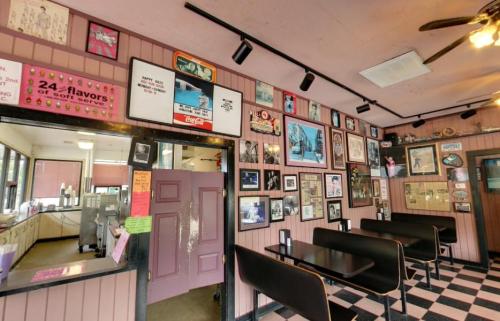 Interior of a retro diner with checkered floors, framed photos on the walls, and seating along the sides.